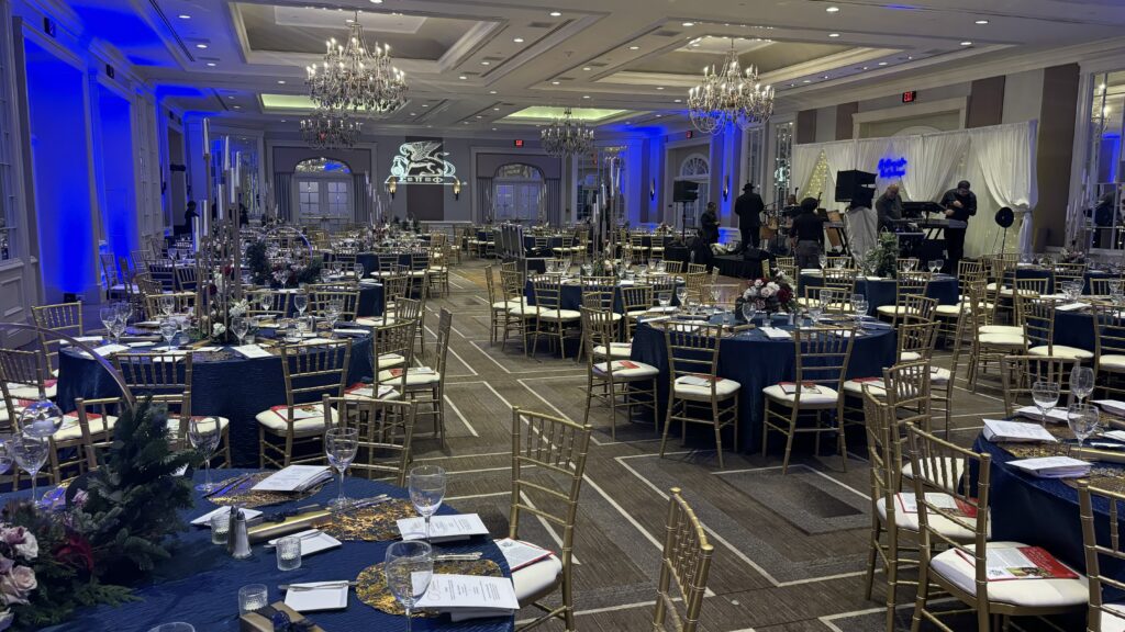 Elegant winter ballroom event setup with gold Chiavari chairs, round banquet tables, blue uplighting, and formal place settings