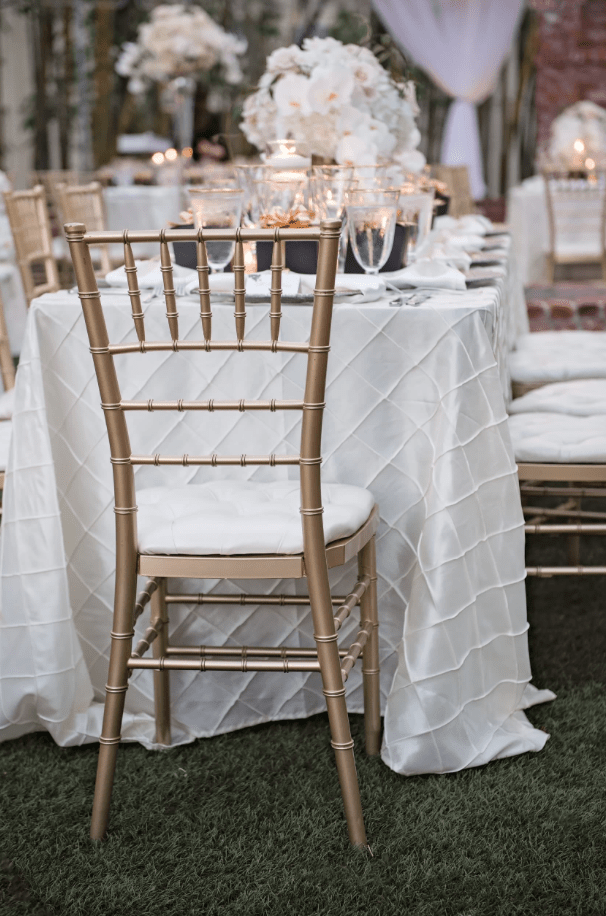 Gold Chiavari chairs with white cushions arranged around round reception tables inside an elegant ballroom with columns, candles, and floral centerpieces. A polished seating style for weddings and formal events in Middlesex, NJ.